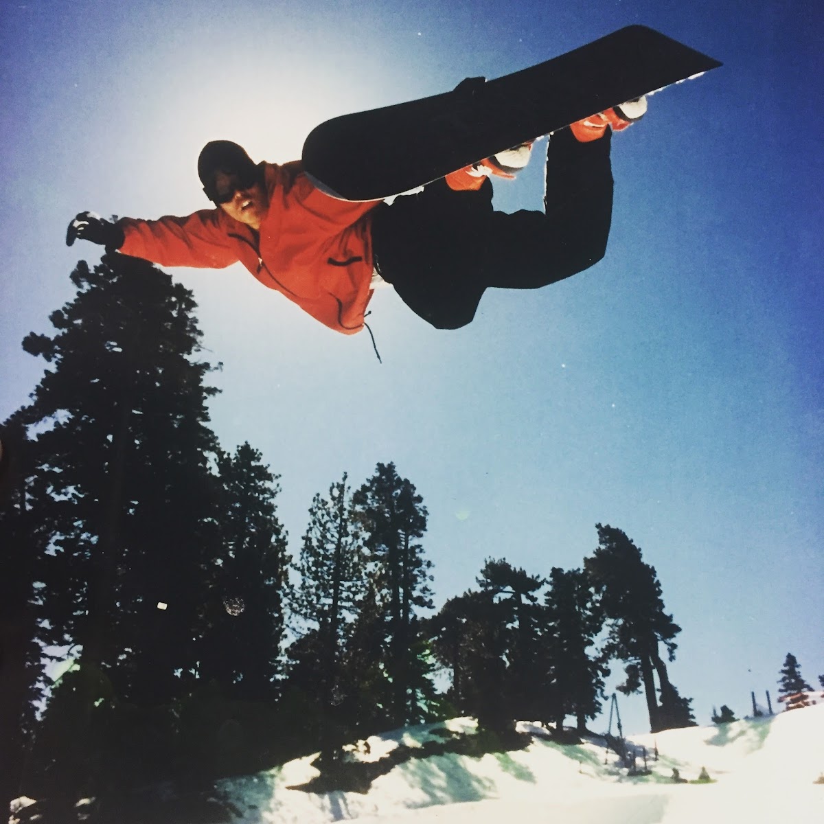 Brent Futagaki grabbing his snowboard mid-air on a method jump against a clear blue sky — his riding days